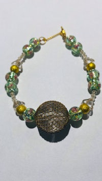 a green and gold beaded bracelet on a white background