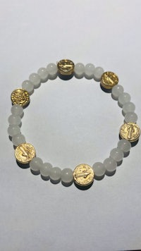 a white stone bracelet with gold coins on it